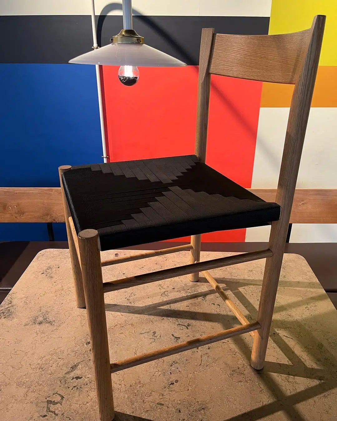 F Chair fra Brdr. Krüger med træstel og sort vævet sæde, set fra skrå side på bord.
