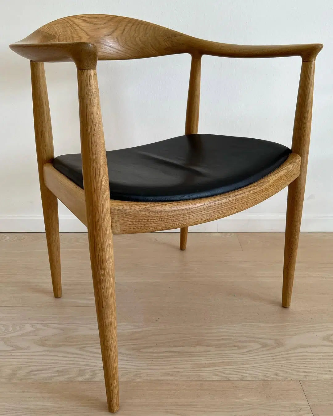 PP501 The Chair i lyst træ med sort polstret sæde set fra siden, viser stolens elegante buede ryg.