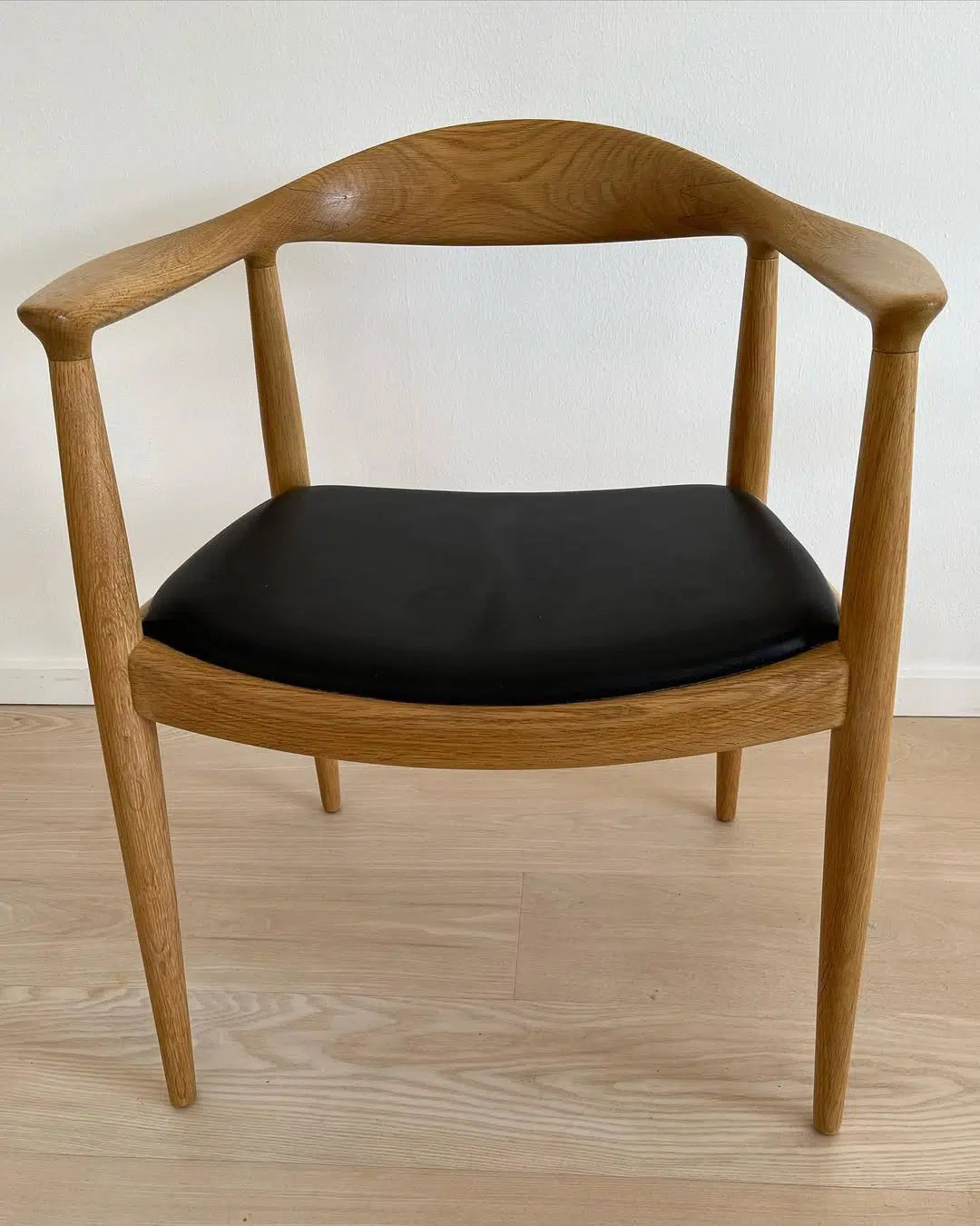 PP501 The Chair med lys træramme og sort polstret sæde, set forfra på lyst gulv.