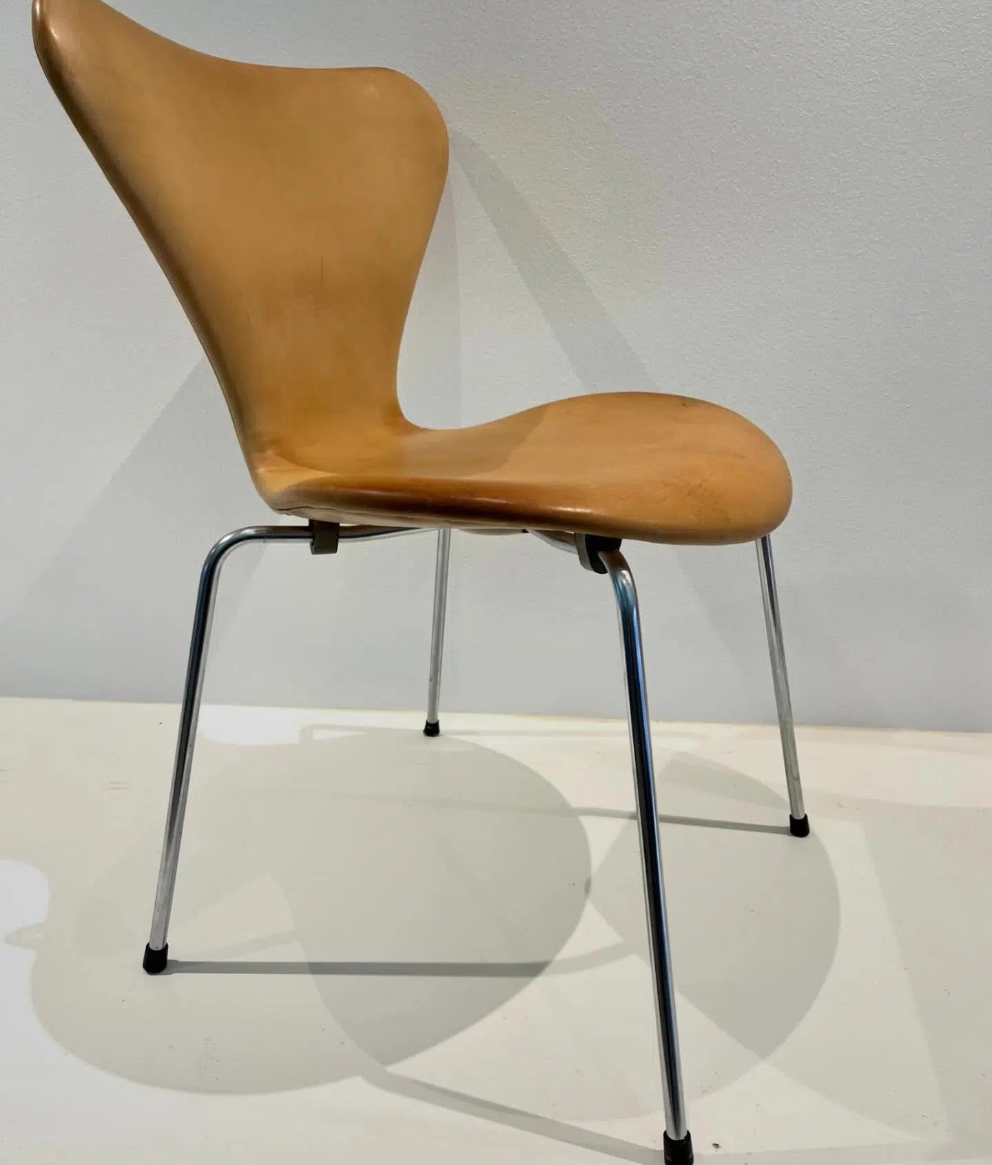 Syverstol eller 7'er stol med polstring i lyst læder og forkromede ben, designet af Arne Jacobsen.